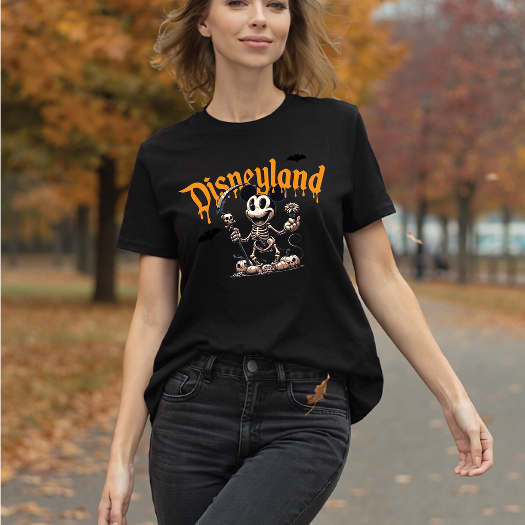 A woman wearing a black Disneyland graphic t-shirt with a Halloween Mickey Mouse skeleton design, walking outdoors on a path with autumn trees in the background.
