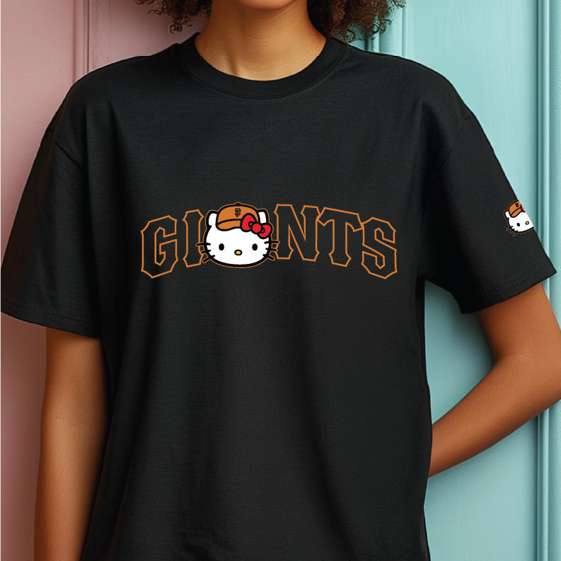 A person wearing a black short-sleeve T-shirt with a Sanrio Hello Kitty graphic. The front of the shirt features the word 'GIANTS' in arched orange-outlined letters, with the 'I' replaced by a white Hello Kitty face wearing an orange cap and red bow.