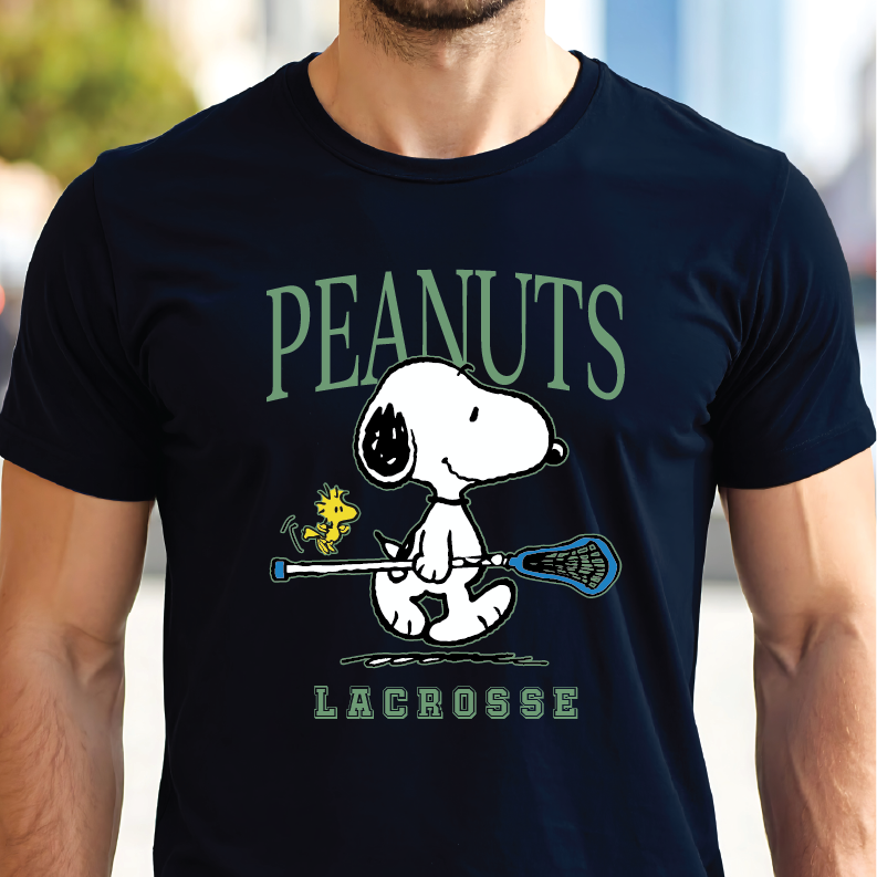 A man wearing a navy blue t-shirt featuring a graphic of Snoopy holding a lacrosse stick with the text 'PEANUTS LACROSSE' in green.